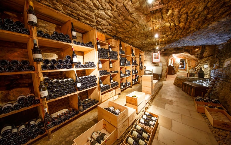 Rustic underground stone wine cellar featuring wooden racks and crates filled with aged wine bottles.