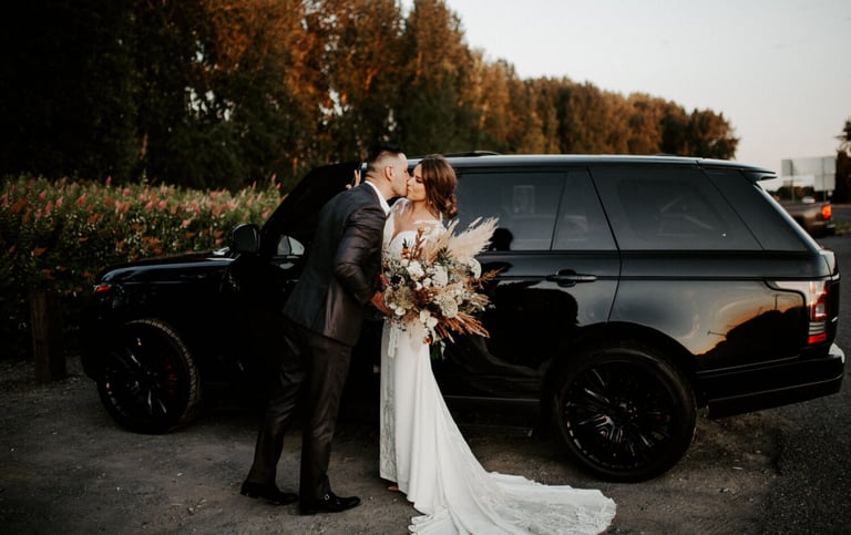 Elegant black luxury SUV with a bride and groom sharing a romantic kiss, perfect for wedding transpo