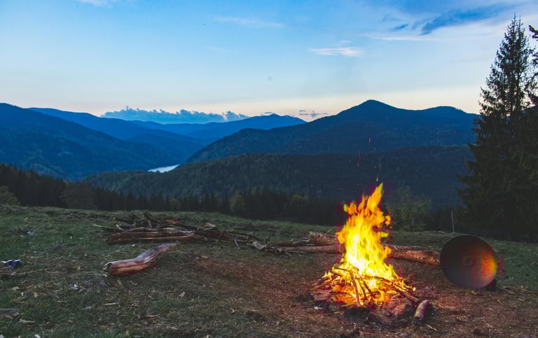 Campfire burning on mountain ridge at sunset, survival warmth, outdoor cooking, and wilderness shelter