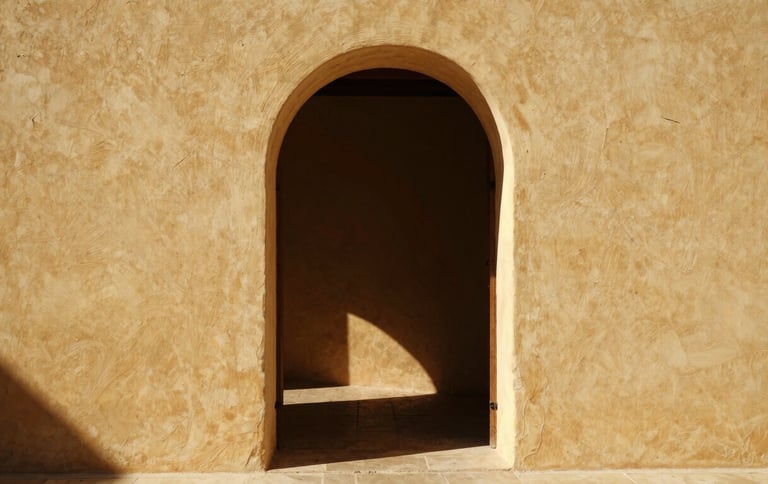 Warm editorial photograph of a rustic Mallorcan interior, sunlight streaming through an open arched doorway, lime-washed walls, minimalist aesthetic.