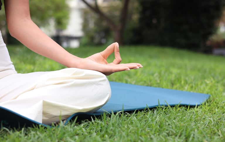 A woman practicing yoga and meditation on a blue mat in a lush green park.