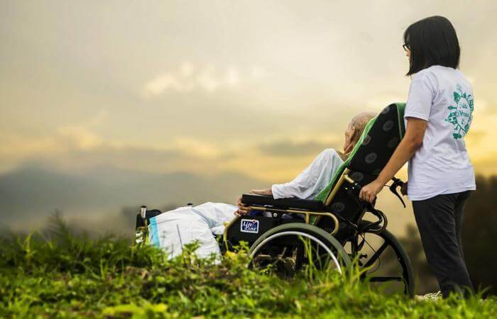 Caregiver pushing an elderly person in a wheelchair outdoors at sunset.