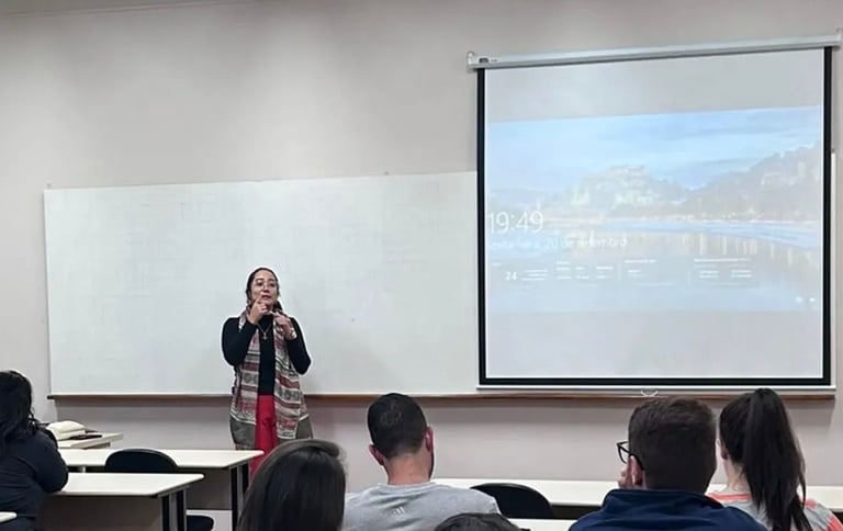 Female professor leading a university lecture in a classroom with students and a projector screen.