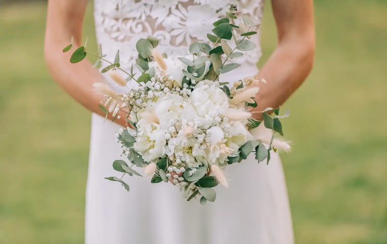 La mariée tient un bouquet de mariée champêtre composé de pivoines blanches, de gypsophile.