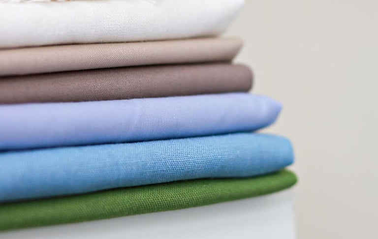 Close-up of a neatly stacked pile of folded fabric swatches in various neutral and pastel colors, including white, beige, bro