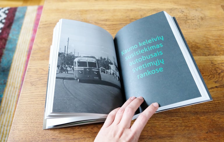 The photo shows the pages of a book being turned. A photograph of a vintage bus and the title of the column "Kaunas passenger