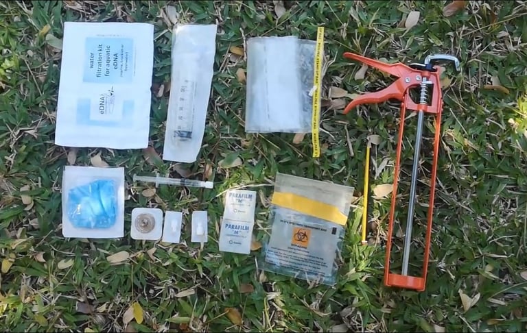 Field eDNA water filtration kit with syringe, parafilm, and sampling tools on grass.