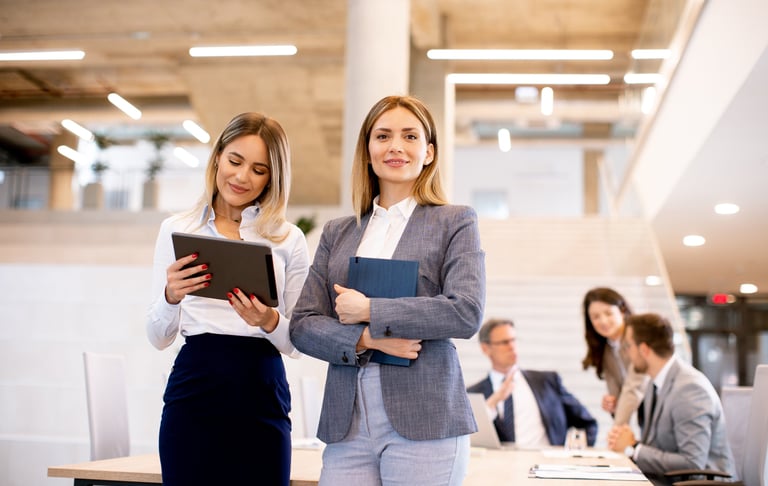 two women in business attire standing in a conference room