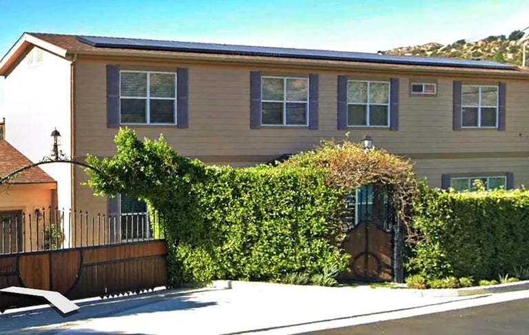 Two story modular home behind front gate and shrubs.