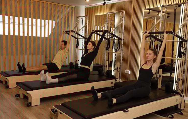 People doing Pilates exercise on tower reformers, pulling up the push-through bar in a studio