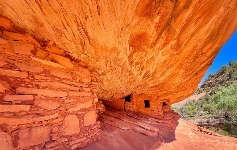 Ancient stone cliff dwelling ruins under a large red sandstone rock overhang in Sedona, Arizona.