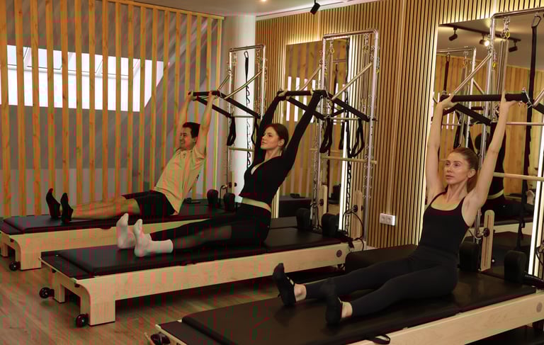 Três pessoas a realizar um exercício de Pilates em reformers torre, puxando a barra push-through