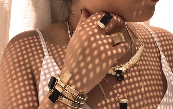 uma mulher usando um mix de colares e de pulseiras pratas e douradas. todas as joias tem um cristal 