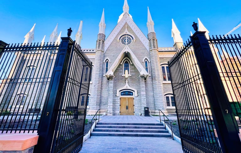 Gothic-style stone assembly hall with white spires behind a wide open black wrought iron gate.