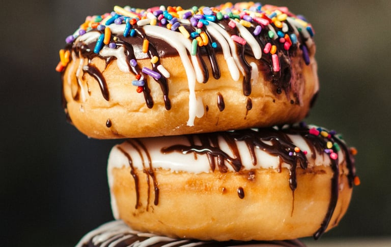 three stacked donuts with white glaze and chocolat coat and colorful sprinkles