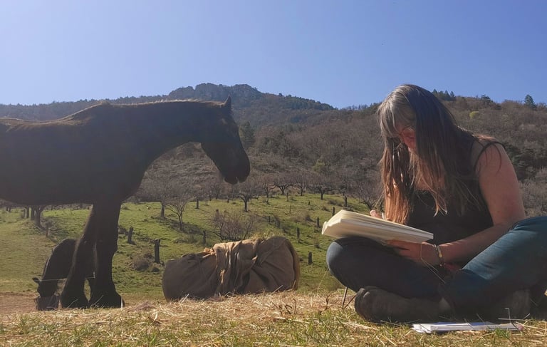 a woman sitting on the grass with a book in her hands and a horse behind her