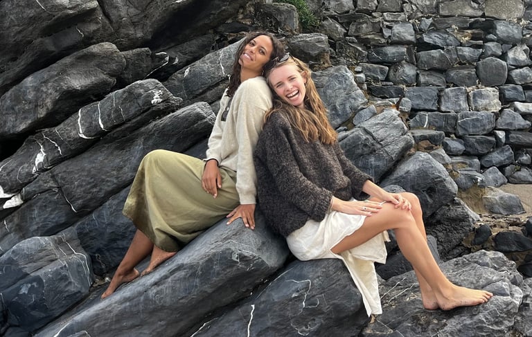 Two women sitting back to back on a rock.
