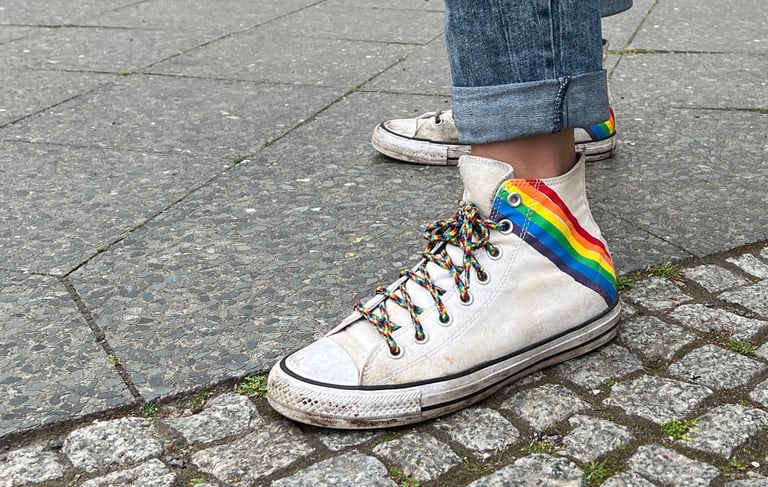 Foto von weißen Turnschuhen mit Regenbogenaufdruck und Regenbogenschnürsenkeln.
