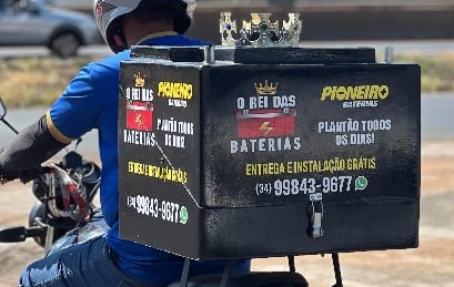 Um entregador segura uma bateria da Disk Baterias Uberlândia em frente a um carro amarelo.