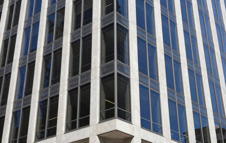 A sharp, professional architectural photograph of a modern steel and glass office building in a North American / US city. The shot is taken from a street-level perspective looking up. Lighting is bright daylight, highlighting clean white concrete and navy blue tinted glass. The composition emphasizes strength and reliability.