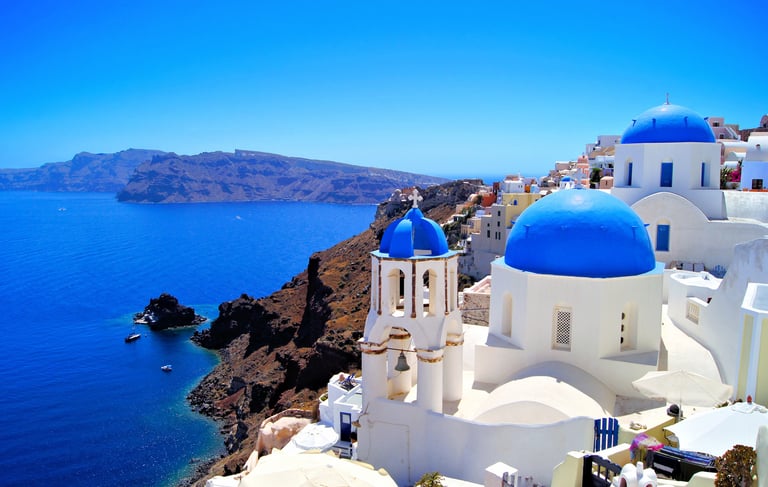 Iconic blue domed churches in Oia Santorini overlooking the Aegean Sea and caldera cliffs.