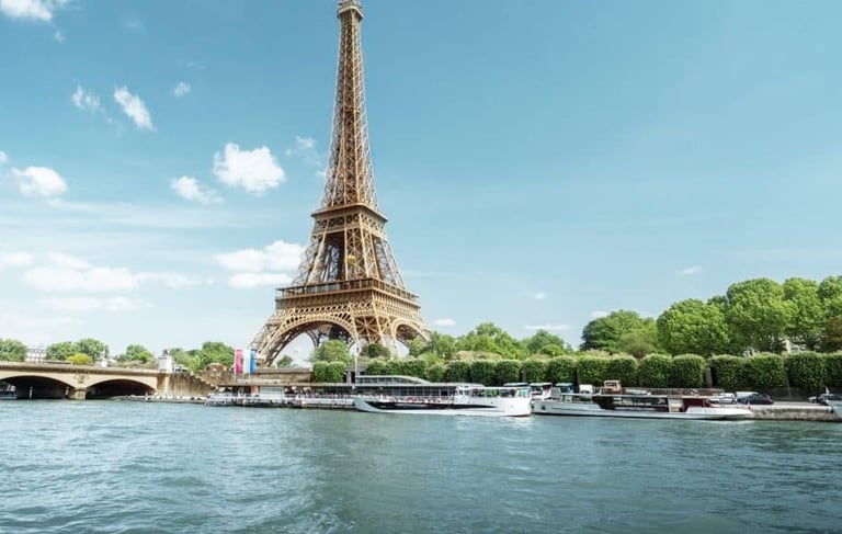 The Eiffel Tower stands tall over the Seine River in Paris with tourist boats docked nearby.