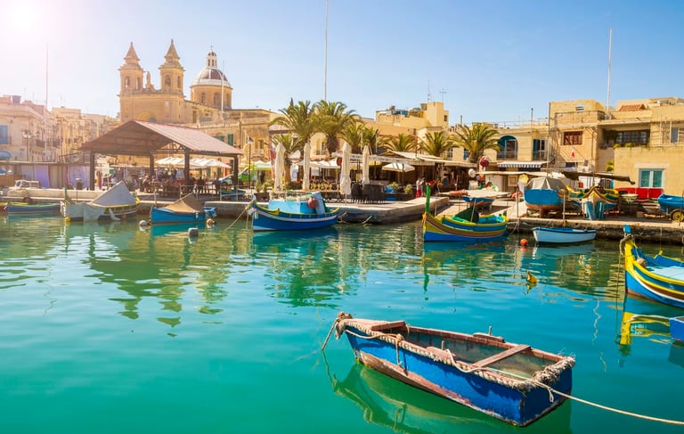 Colorful Luzzu fishing boats in Marsaxlokk village harbor, Malta, on a sunny day.