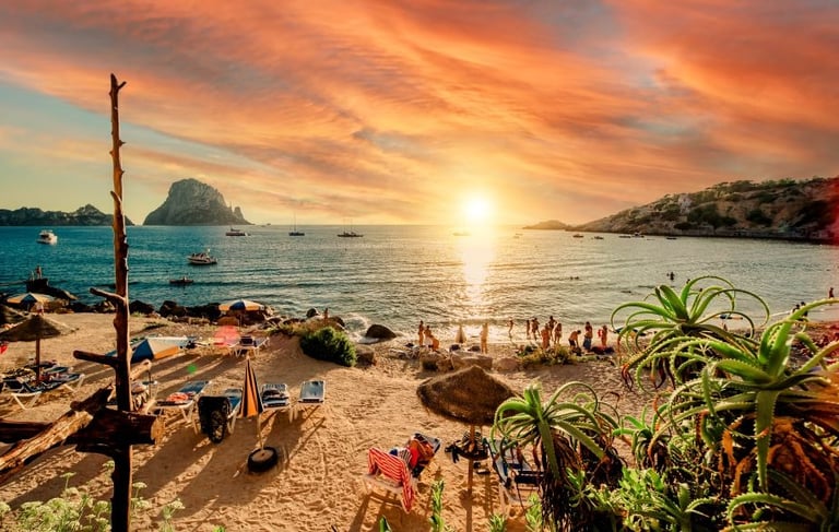 Golden sunset over Cala d'Hort beach in Ibiza with views of Es Vedra island and boats.