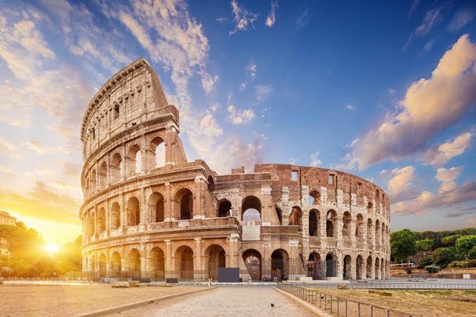 Sunset over the Roman Colosseum with a golden sky and wispy clouds in Rome, Italy.