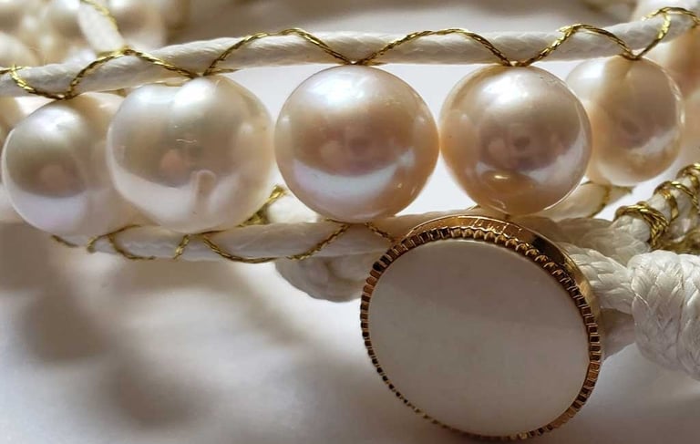 a bracelet with a white pearl and a gold cord