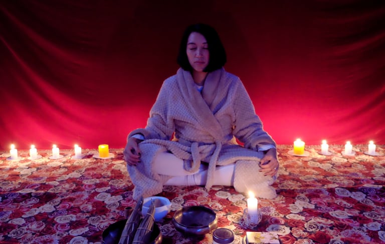 an asian woman on a meditative state with plenty candles on the back and ritual tools infront
