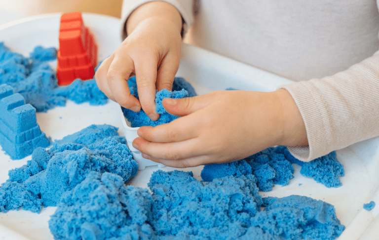 a child's hands holding a toy with blue sand