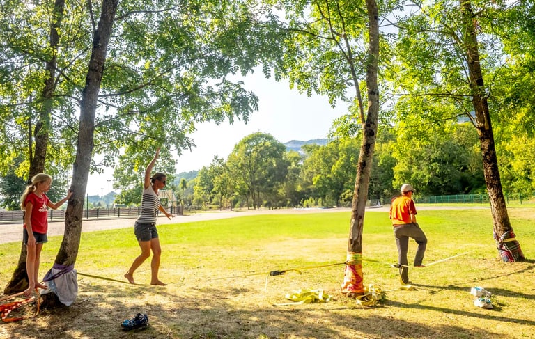 Deux adultes et une enfant pratique la slackline dans un parc