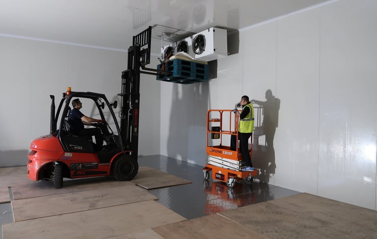 Forklift lifting a large industrial evaporator inside a freezer room during installation process