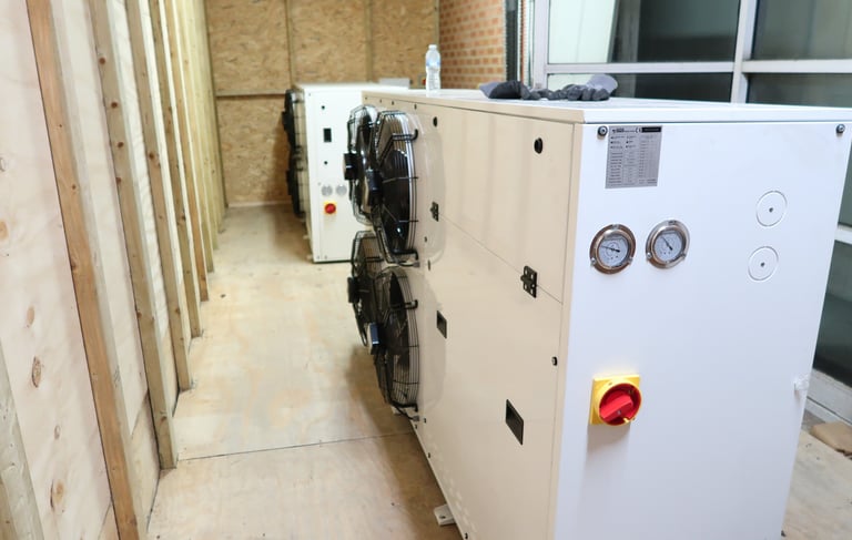 Two large industrial condensers in a commercial freezer room, with one serving as a backup spare uni