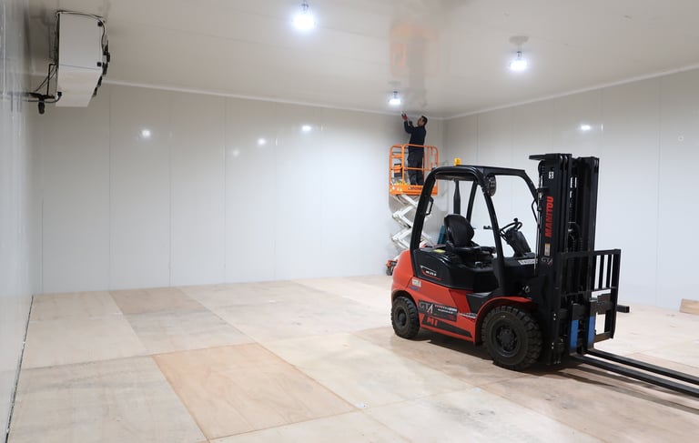 Scissor lift positioned inside a large industrial freezer room, used for instaling of high-mounted