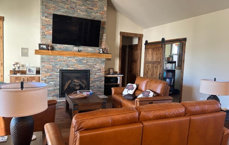 a living room with a couch and a television, and stone fireplace - made by Saddle Horn Custom Homes