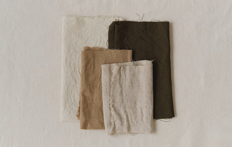 Neutral folded linens stacked on fabric, symbolizing simplified belongings and gentle decluttering.