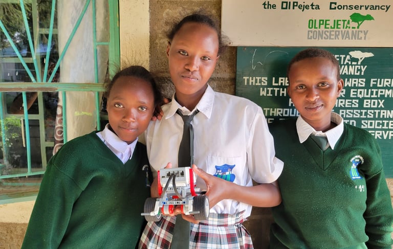 3 kenyan girls in school uniforms, holding a robot