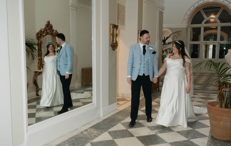 A bride and groom holding hands walking past a mirror in an elegant wedding lartington hall.