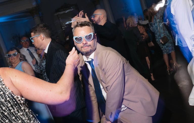 Wedding guests wearing fun heart-shaped sunglasses dancing at a relaxing evening reception party.