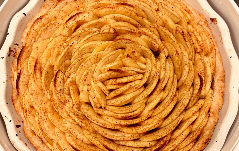Freshly baked homemade French apple tart with cinnamon-dusted slices arranged in a rose pattern.