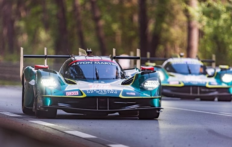 Aston Martin Valkyrie AMR Pro hypercars racing on a track through a forest at sunset.