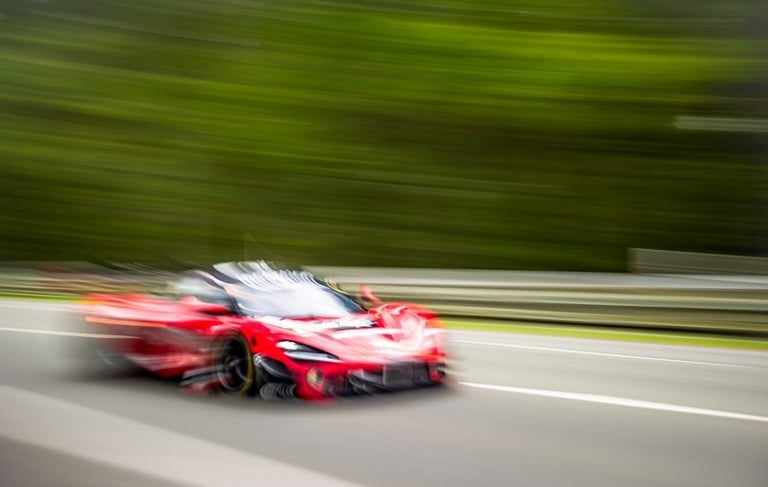 Motion blur of a red supercar speeding on Nurburging track with green forest background.