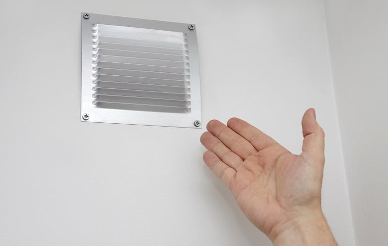 a hand holding a small metal venting venting in a bathroom