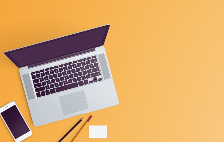 An overhead shot of a vibrant sherbert orange surface with an open laptop, cell phone, pens/pencil