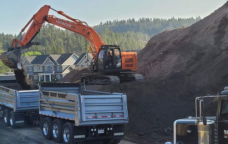 a truck with a large load with an excavator adding to the dirt