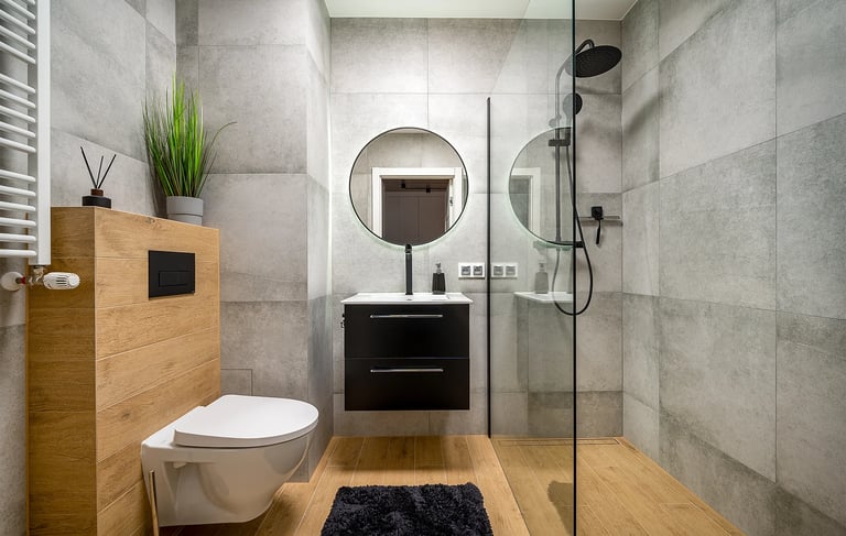 Nowoczesna łazienka z prysznicem walk-in, toaletą, umywalką i okrągłym lustrem.