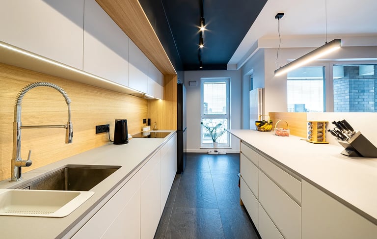 Nowoczesna kuchnia z białymi szafkami, drewnianym blatem i wyspą kuchenną.