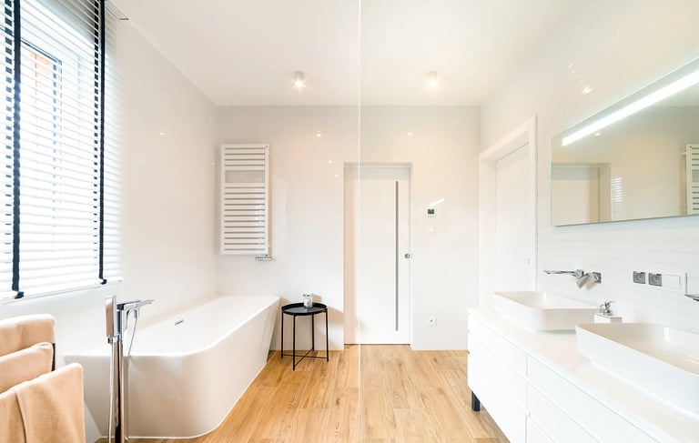 Jasna łazienka z wolnostojącą wanną, podwójną umywalką, lustrem i drewnianą podłogą